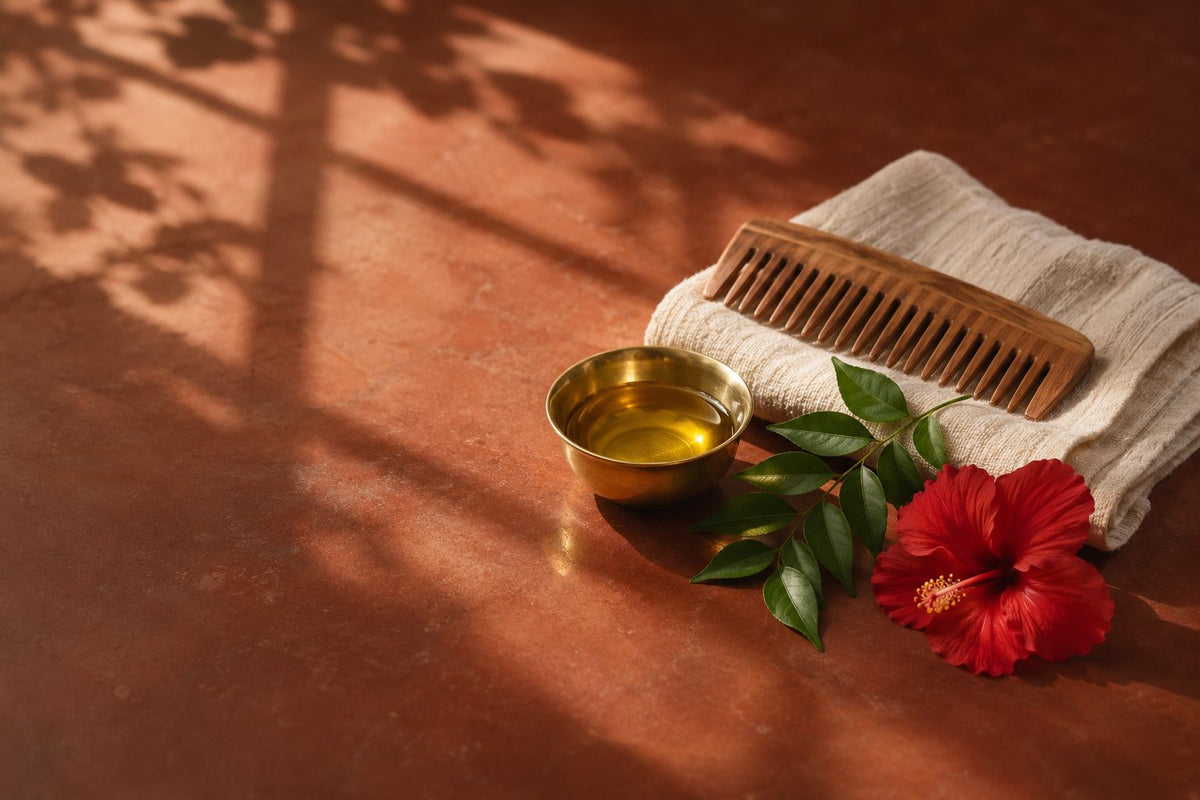 Bowl of warm coconut oil with a wooden comb, hibiscus and curry leaves for a Sunday champi